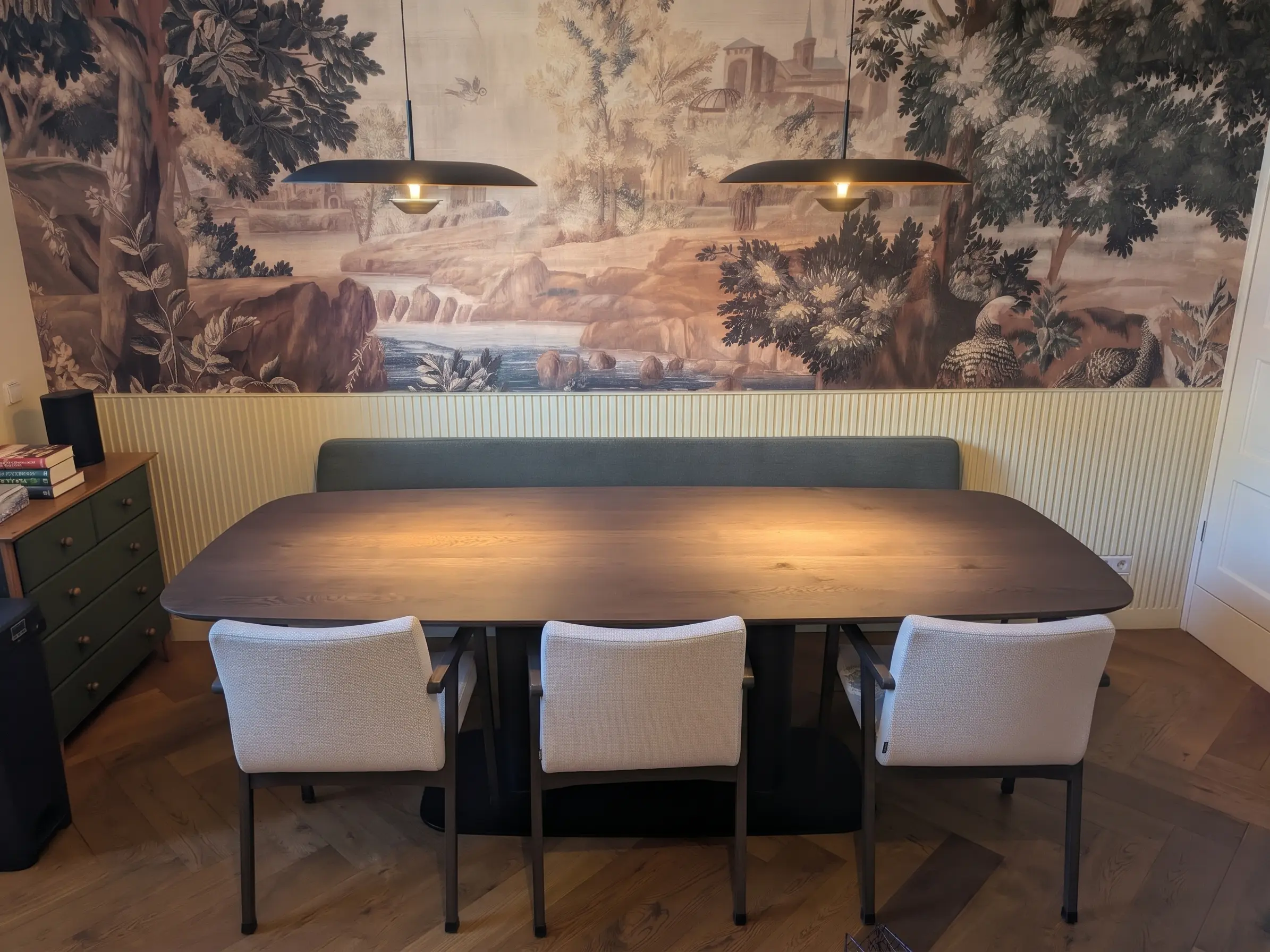 Eetkeuken in Woerden na het interieuradvies, met landschapsbehang van KEK Amsterdam, lambrisering en een groene eetkamerbank aan een donkere houten tafel